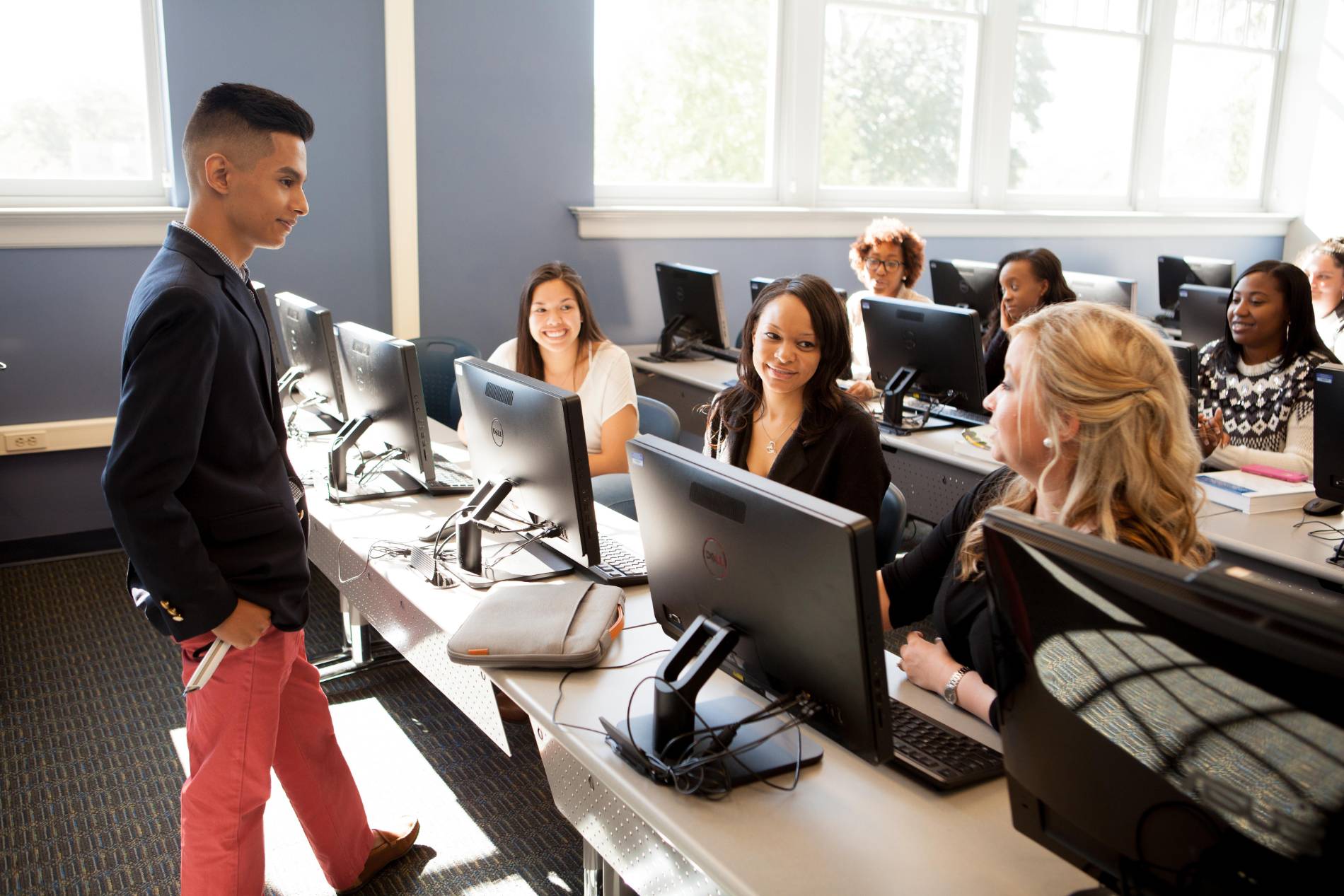 Promotional photo of students participating in instruction in a computer classroom at Spartanburg Community College. The image shows students seated at desktop computers while engaging with an instructor and classmates, highlighting collaborative learning, technology-based education, and student success in an interactive academic environment.