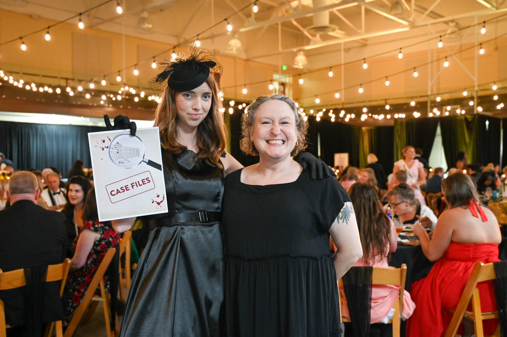 Image of two women one holding a case file prop for the murder mystery dinner.