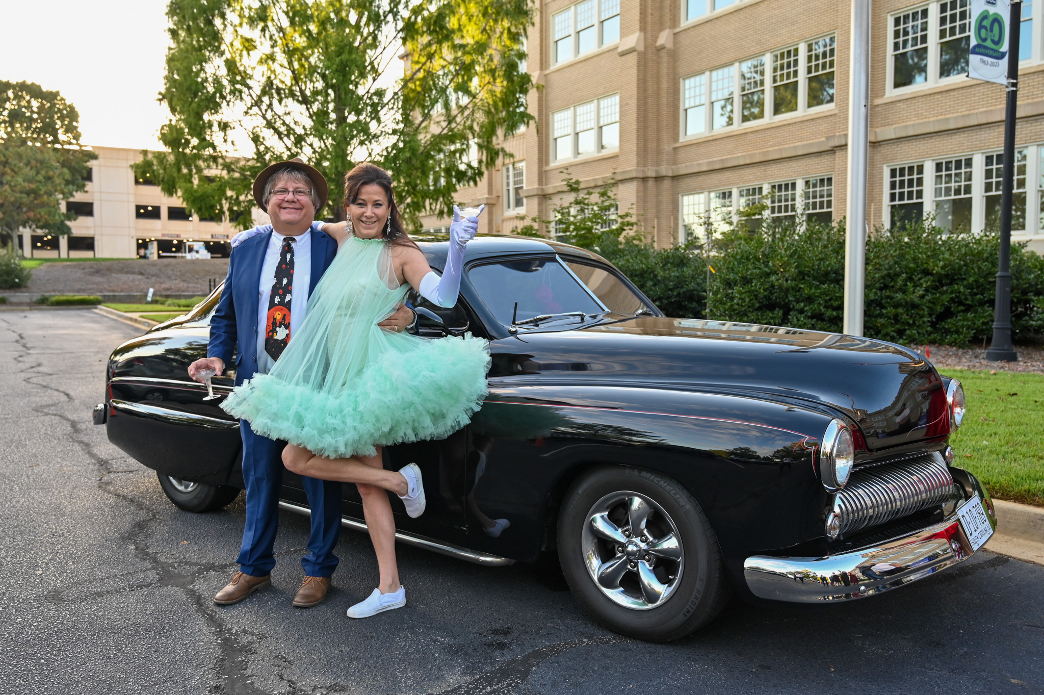 Guests dressed in elegant vintage attire pose beside a classic black car during the Murder Mystery Dinner at Spartanburg Community College. Their timeless looks, complete with pearls, fur, and suspenders, capture the glamour and spirit of the evening’s 1940s-inspired theme.