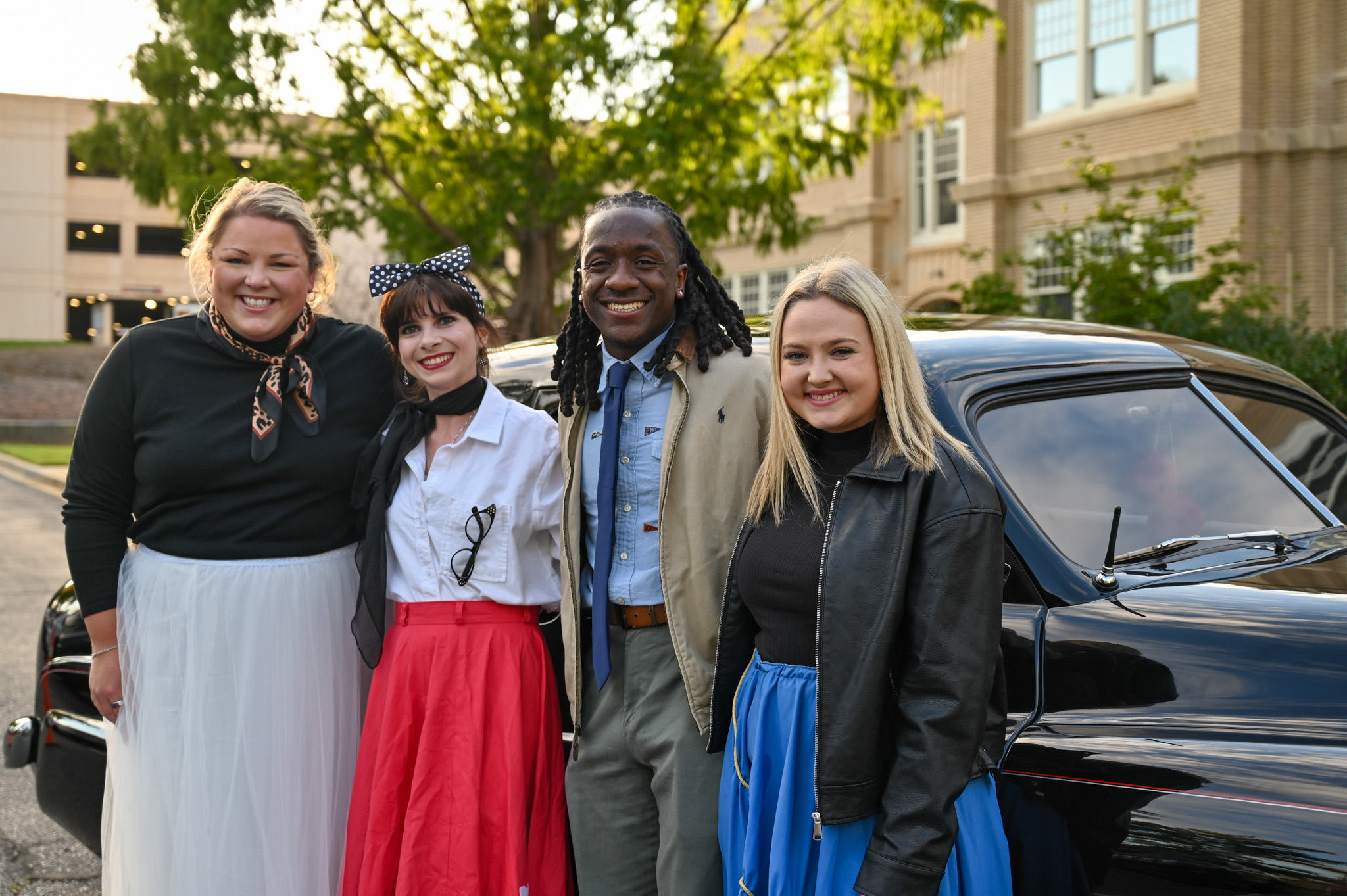 Guests enjoy the Murder Mystery Dinner at Spartanburg Community College, posing beside a vintage black car in elegant retro fashion. The four people's stylish outfits and cheerful expressions capture the lively, nostalgic atmosphere of the college’s 1940s-themed evening event.