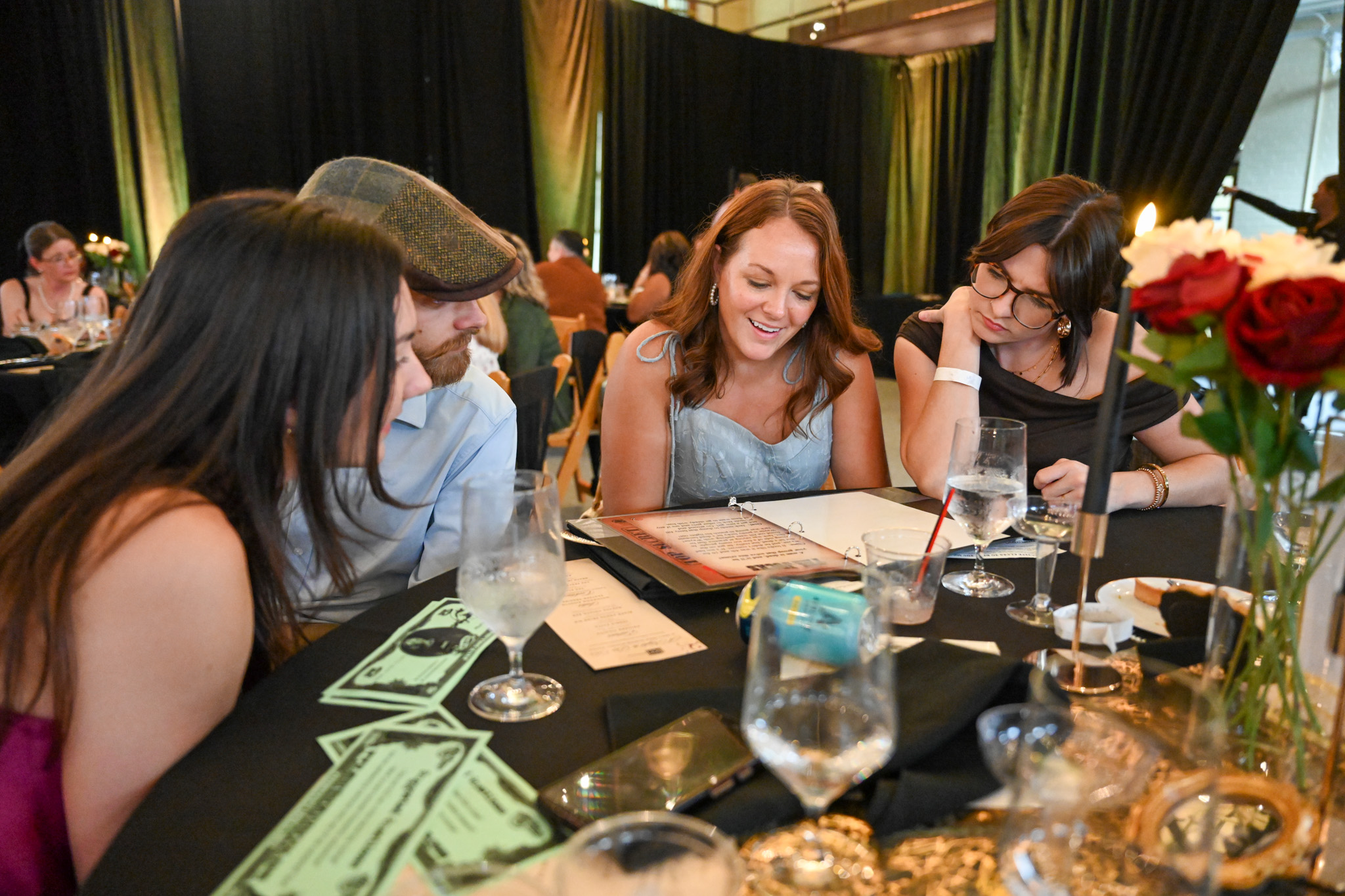 A group of four stylish people at the dining table hovered over the case file to try and solve the murder mystery game