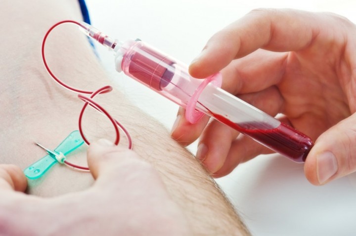Close-up of a healthcare professional drawing blood from a person’s arm using a syringe, with blood visible in the barrel and a catheter inserted into the vein.