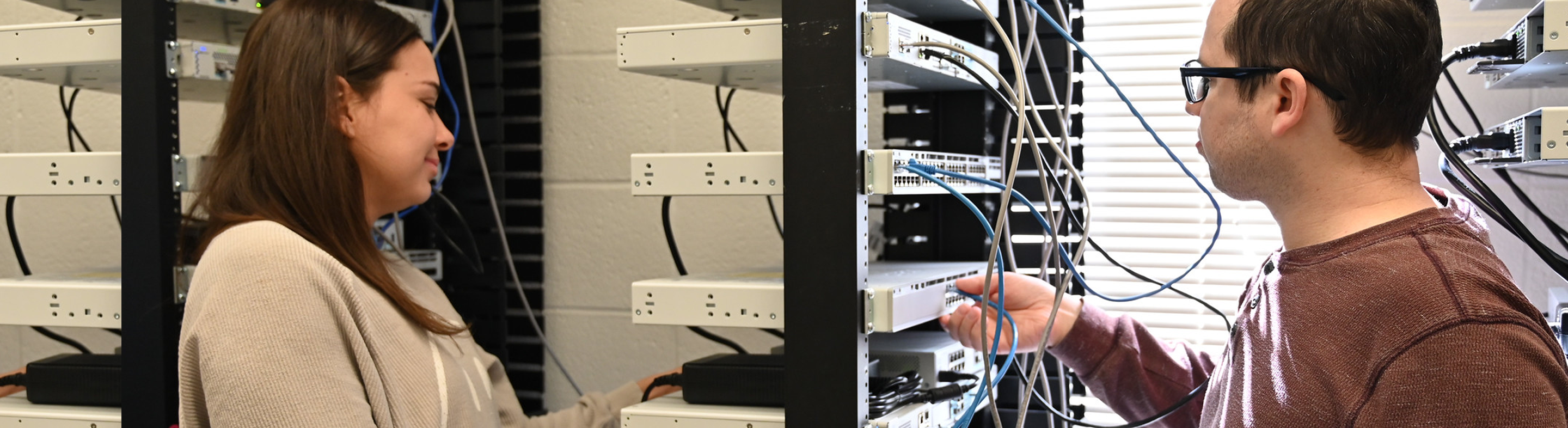 Two students work on a server rack, connecting cables and configuring network equipment in a technology lab.