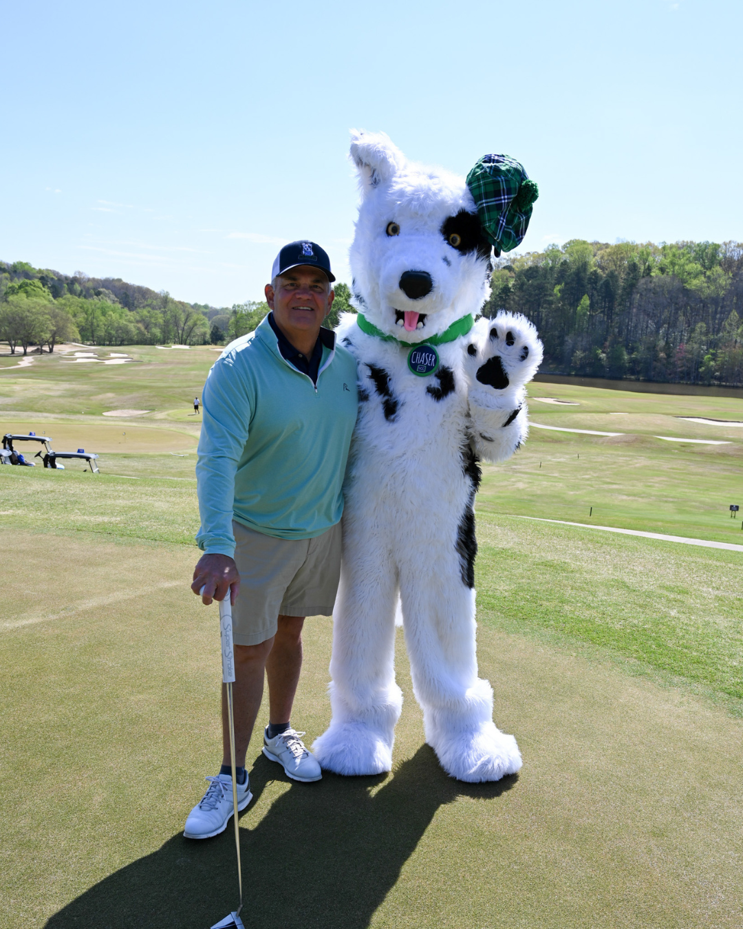 An older man in golf attire poses with Chaser the mascot