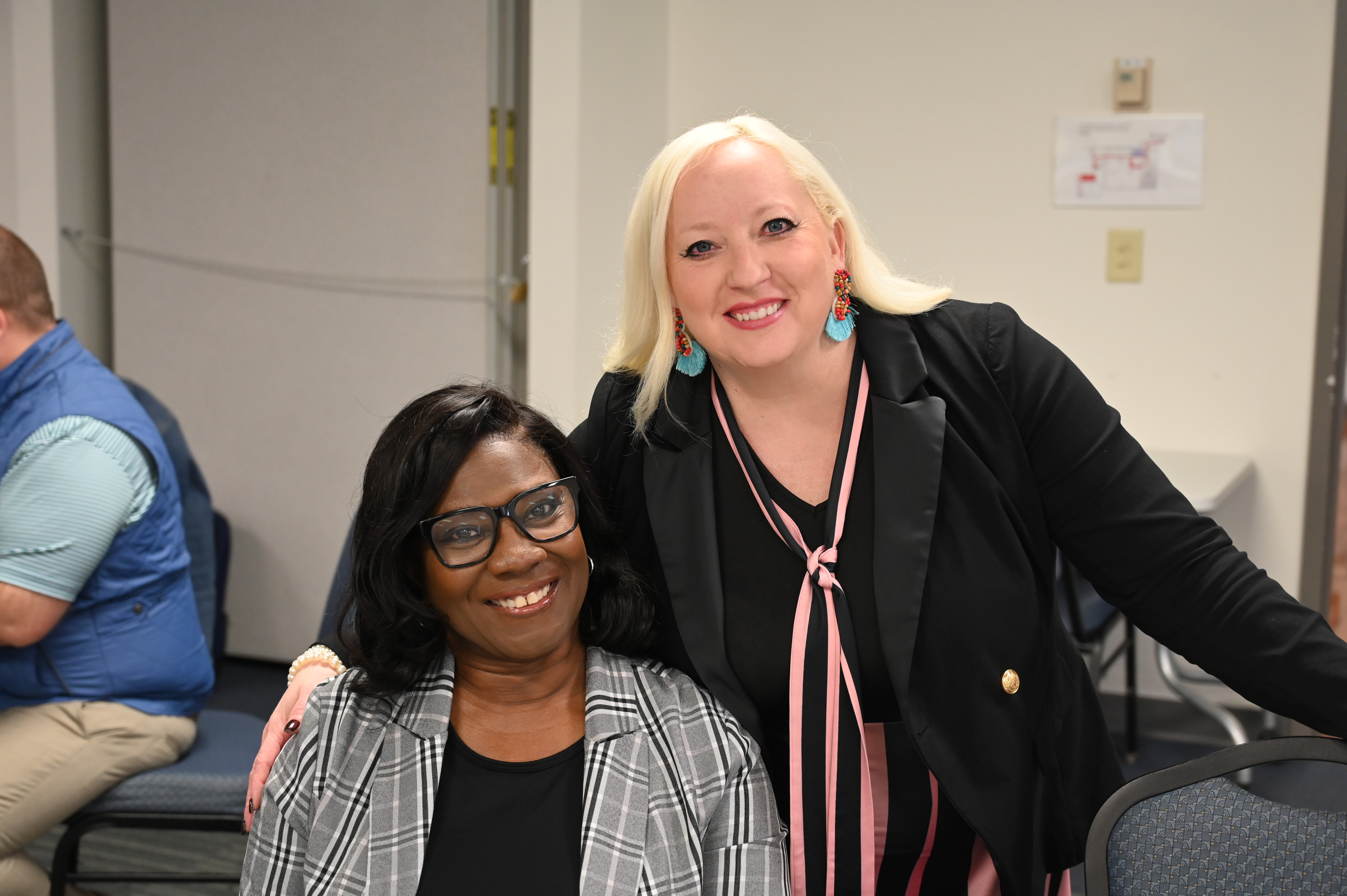 Two women in business professional attire smile and pose for a photo.