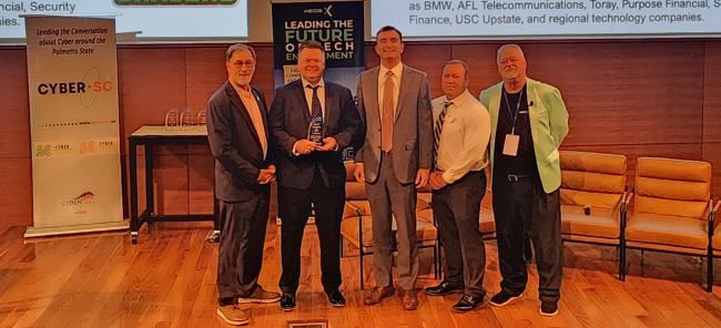 Group of professionals standing on a stage at a cybersecurity and technology conference, presenting an award during a CyberSC event focused on innovation, workforce development, and the future of technology in South Carolina.
